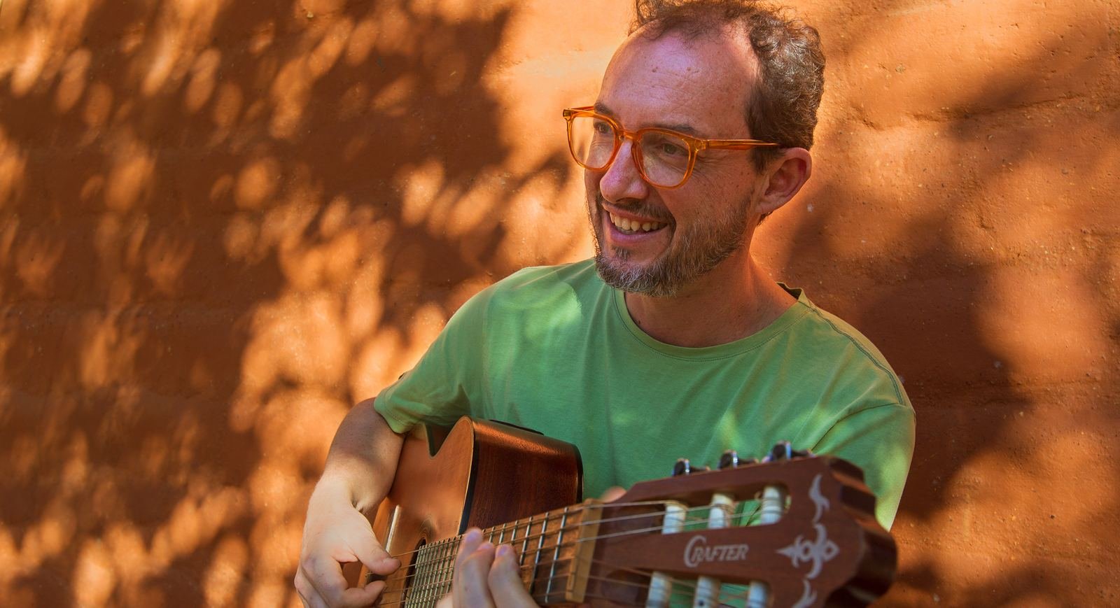 Rafael Longo tocando violão ao ar livre, diante de uma parede de terra
